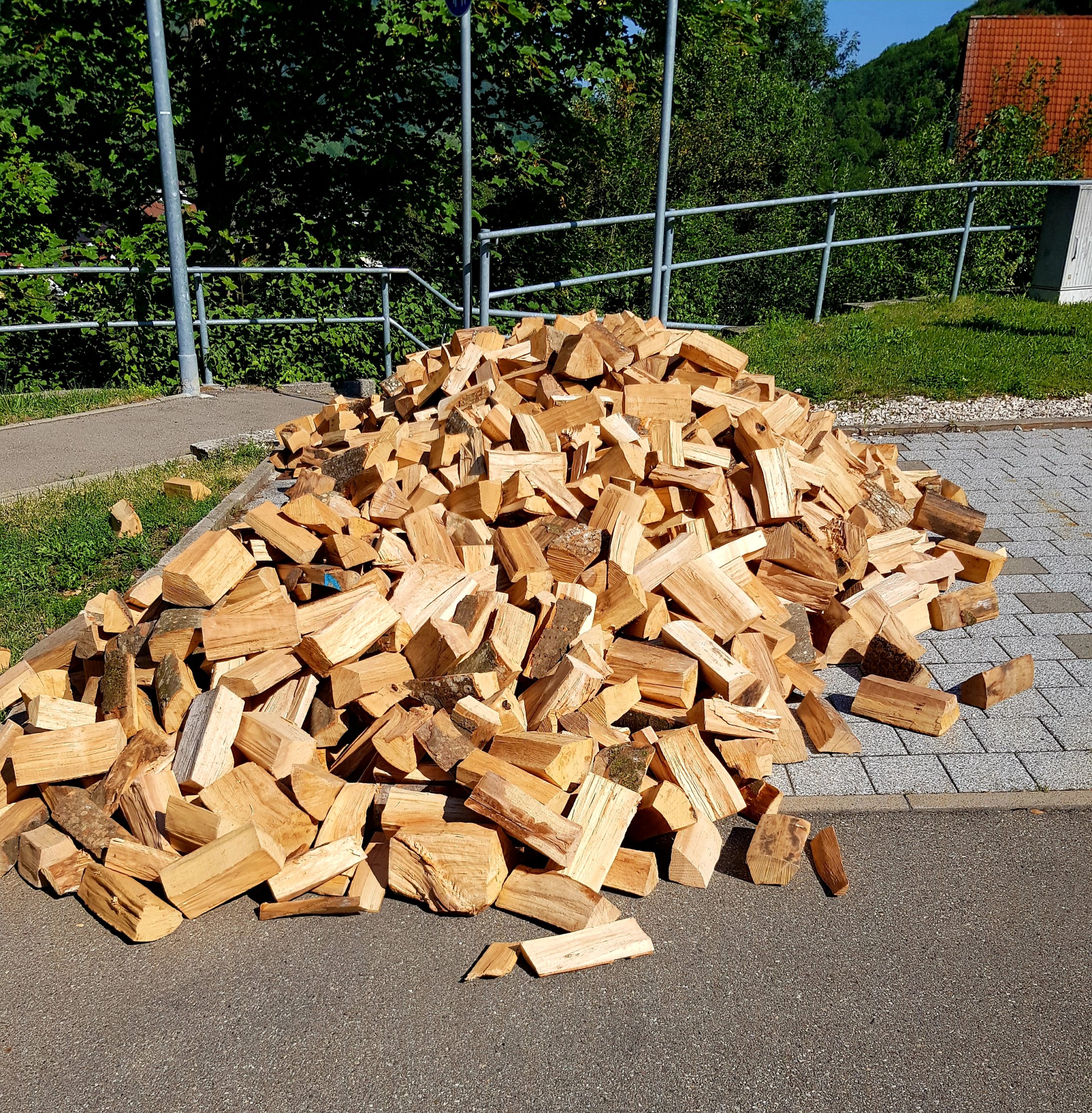 Frisch geliefertes Brennholz auf einem Gehweg, gestapelt in einem großen Haufen, bereit zur Einlagerung oder Nutzung.
