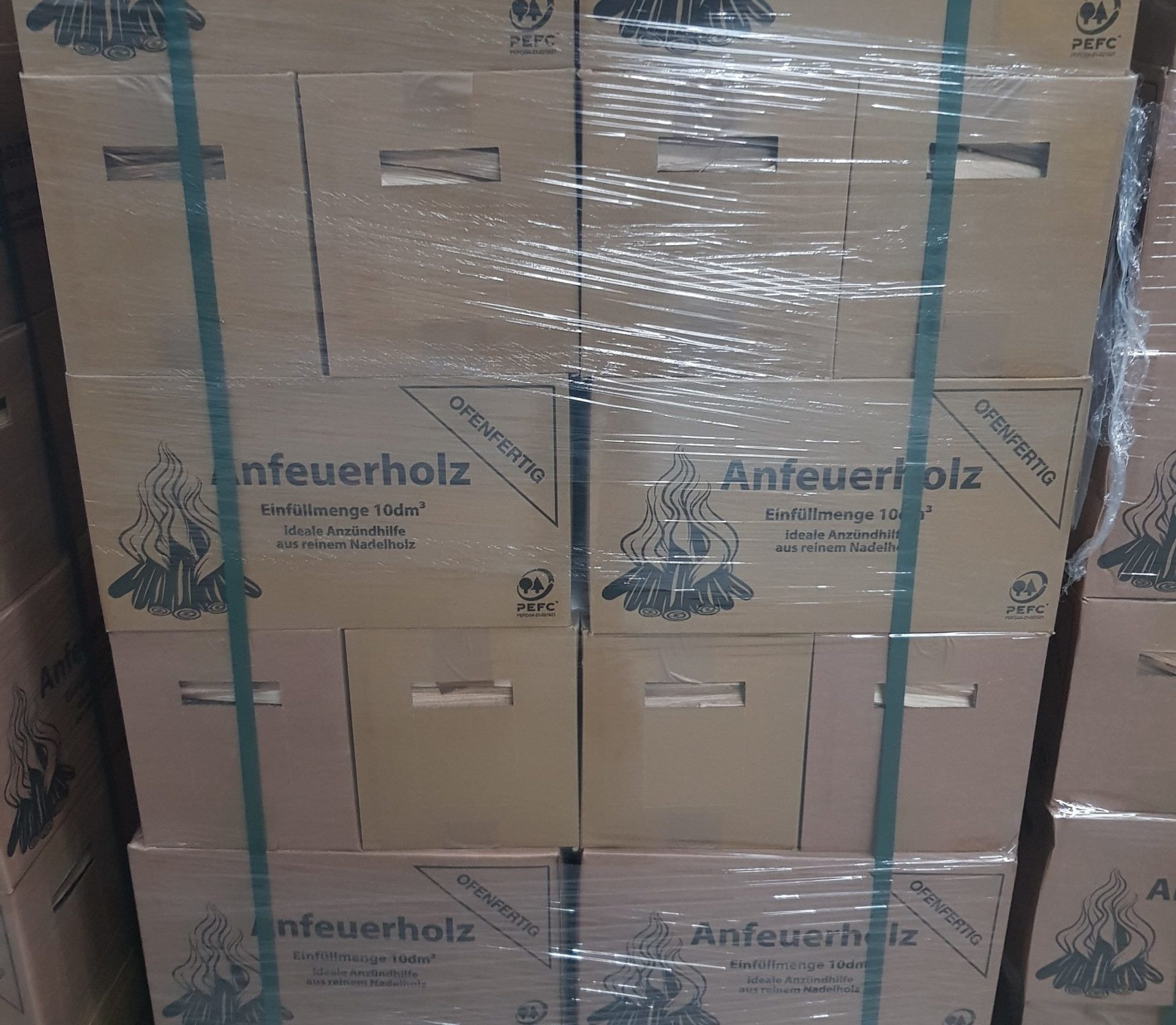 Palette mit Kartons Anfeuerholz, ofenfertig verpackt, in Folie und mit Bändern gesichert.